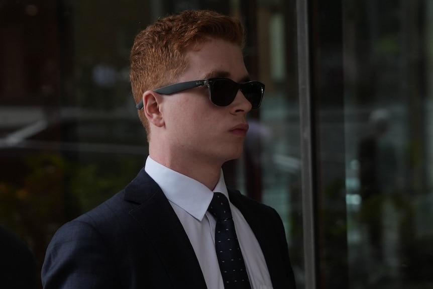A red haired man in dark sunglasses and suit leaves court.