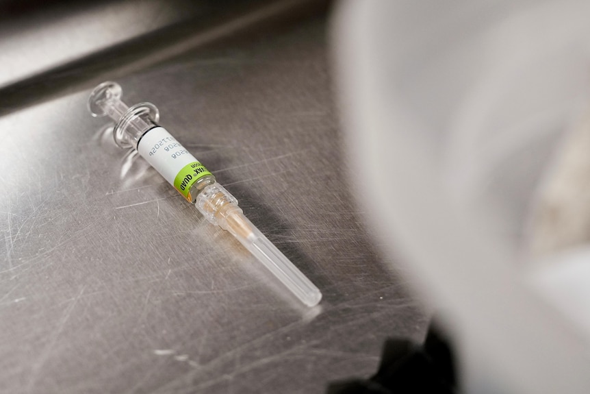 A capped syringe filled with a flu vaccine, resting on a stainless steel surface.