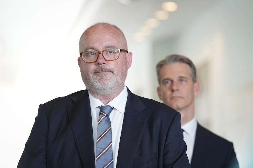 Two middle-aged men in suits standing in a corridor.