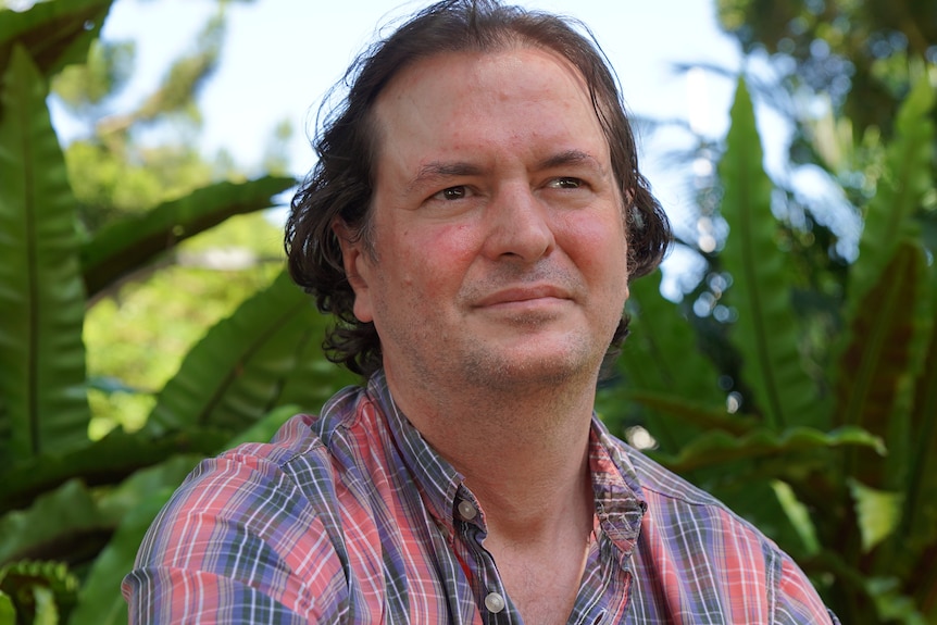 A man with long brown hair wearing a flannel shirt.