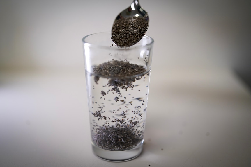 glass of water with chia seeds being poured in with spoon