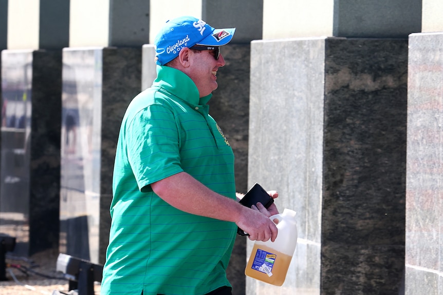 Man walks into court holding jug of juice, smiling