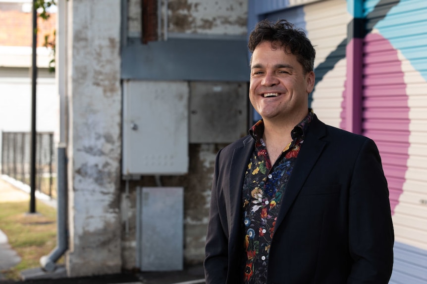 Man smiling in front of artistic mural wall