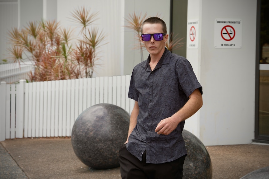 A young man wearing a blue shirt and sunglasses outside the local court