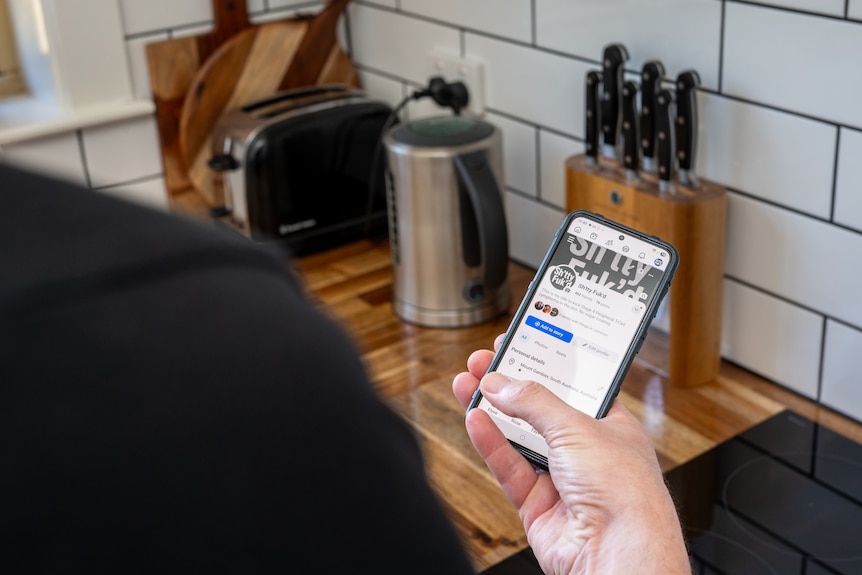 A man holding a phone with a Facebook page open on it.