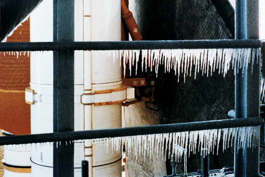 Colour photo of metal girders with rows of icicles hanging off them, and the wing of a space shuttle in the background.