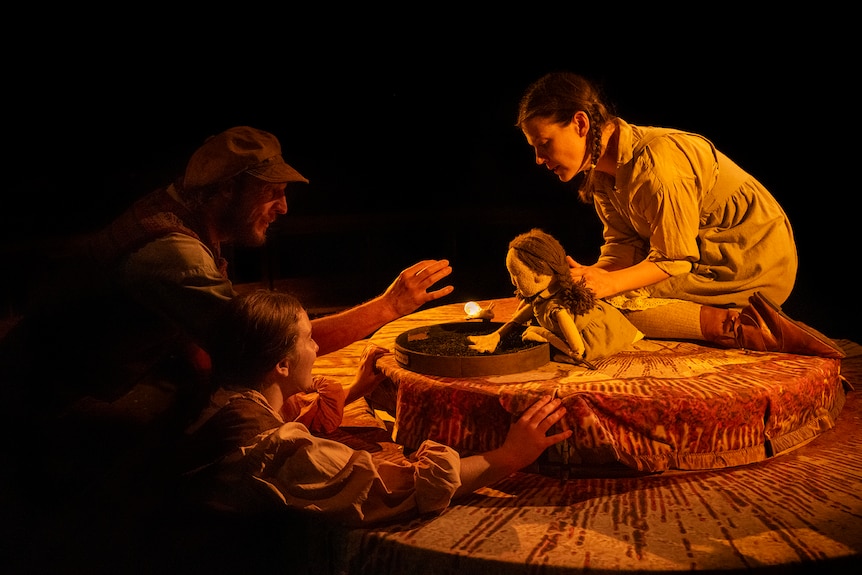 An actor holds a puppet, while two others actors look on