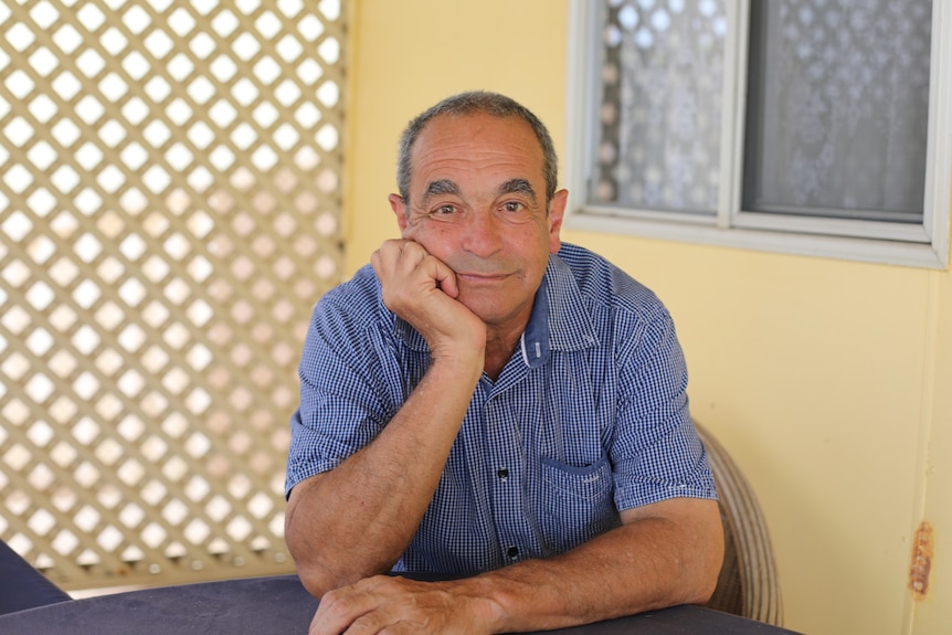 Victor Tanti wear blue shirt, seated, head rests on hand.