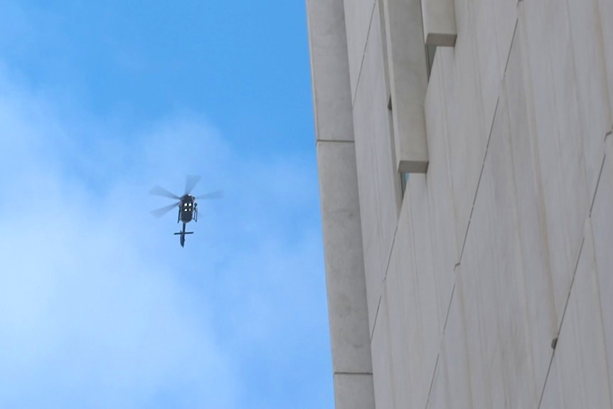 A police helicopter circles a concrete building