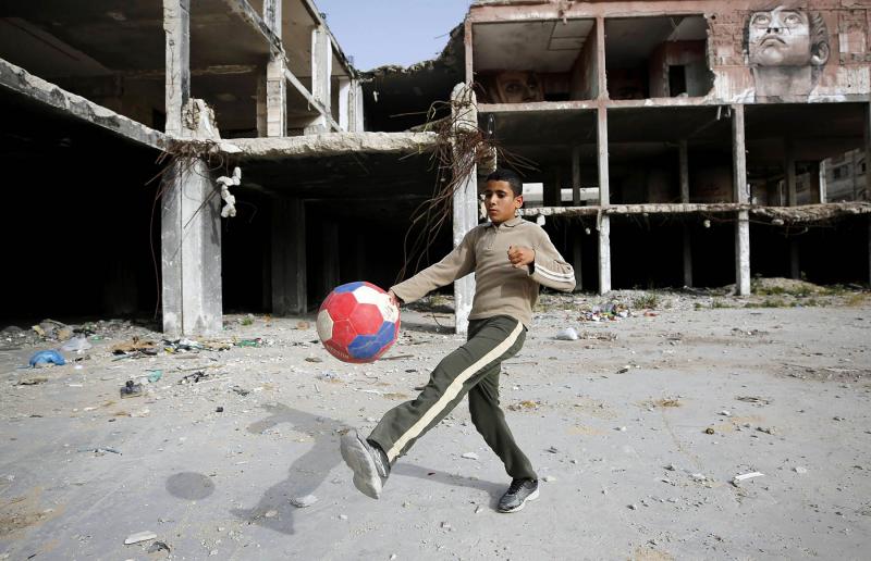 A boy plays football next a partially-destroyed building in Gaza City.