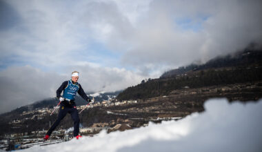 A man in a blue Olympics suit skies on the snow.