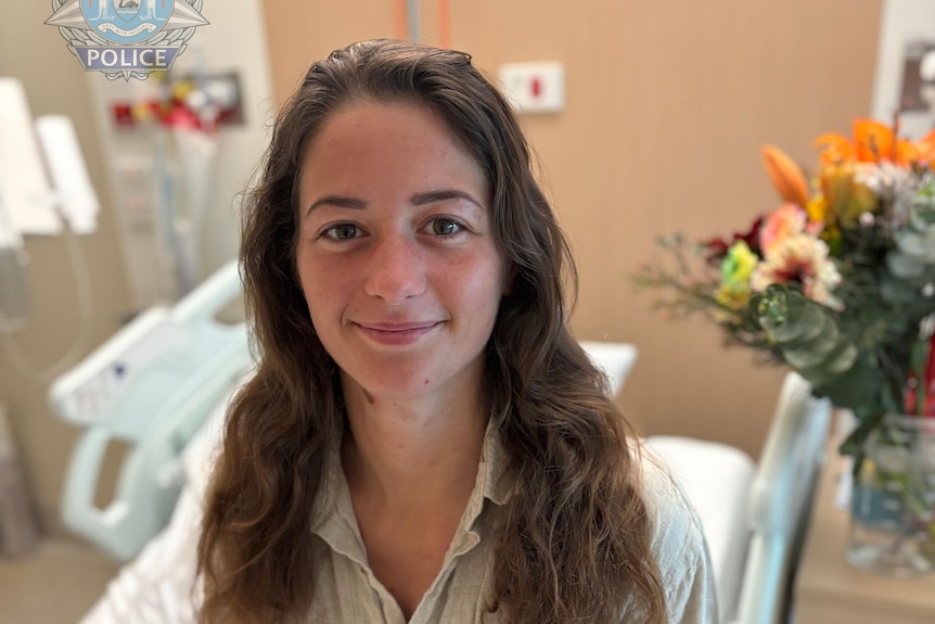 A young woman with long brown hair sitting on a hospital bed.