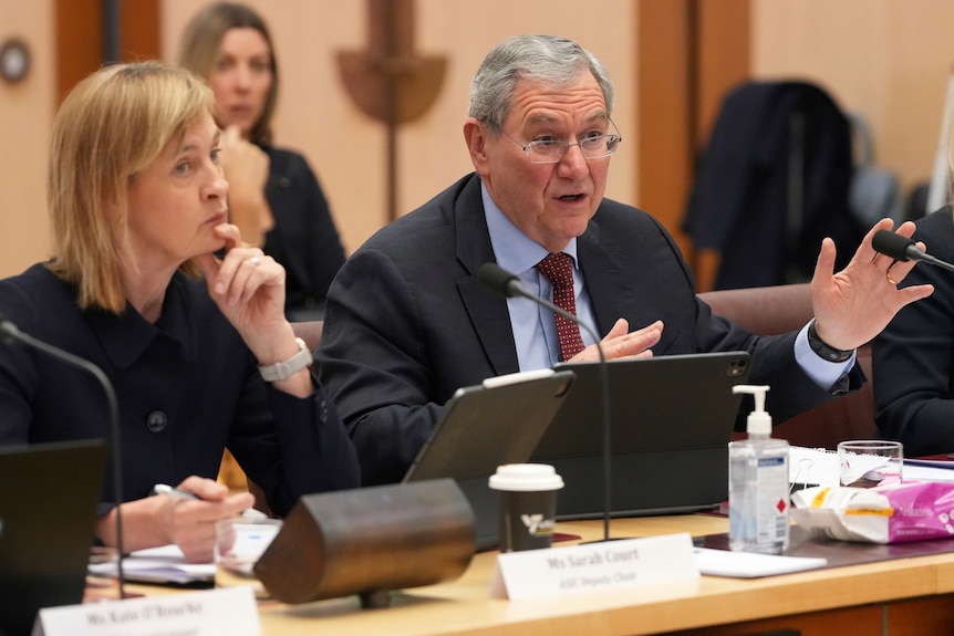 Sarah Court sits looking intently with one hand to her chin while Joseph Longo talks, gesturing with hands.