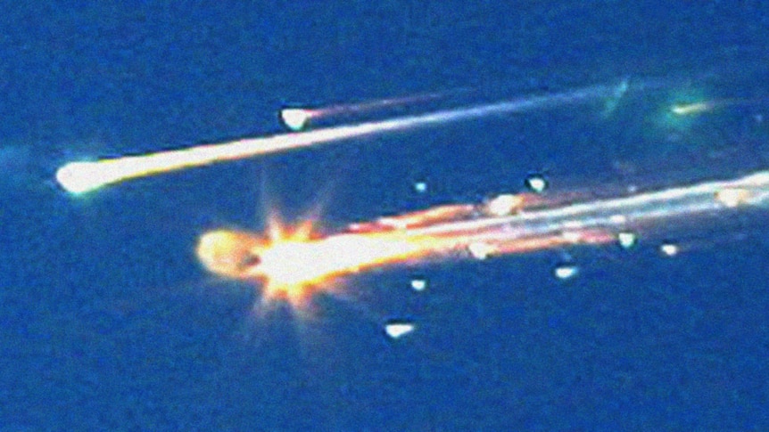 Grainy image of bright streaks, like shooting stars, against a deep blue sky, moving from right to left.