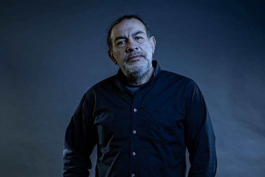 Against a dark background, Khaled Sabsabi stands in dark shirt with shoulders back and face neutral.