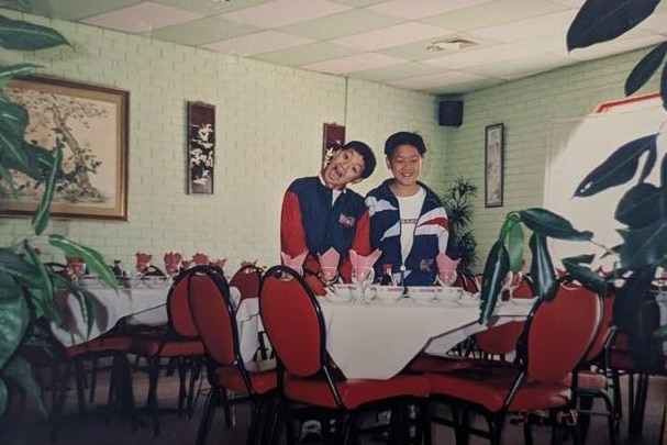 Two young boys standing beside each other. They are both standing behind a round table covered with white sheet.
