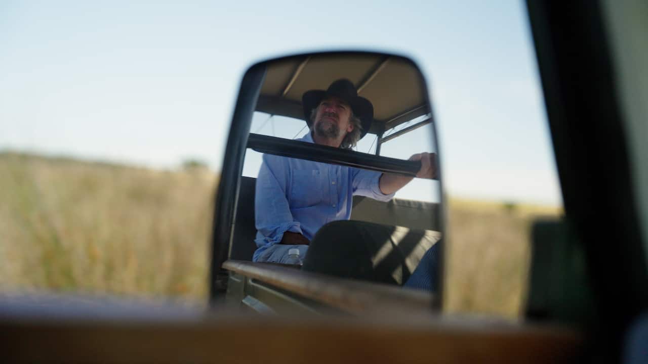View of a man sitting in the back of a vehicle through a rear vision mirror.