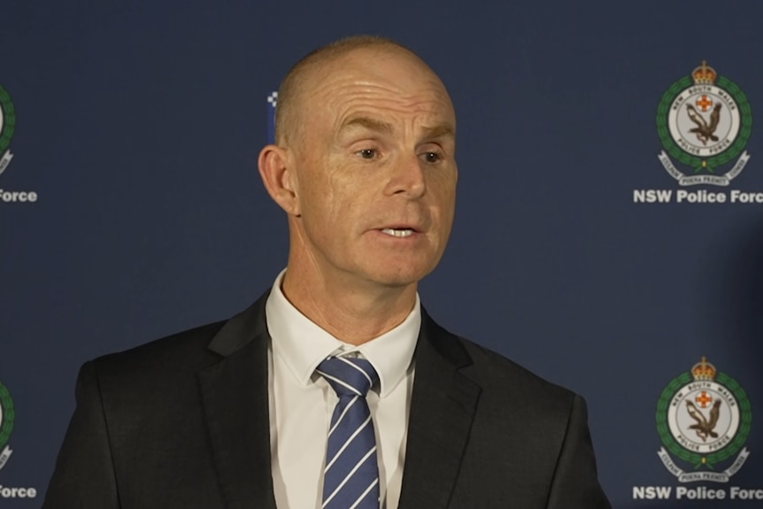 A detective dressed in a suit and tie addresses media.