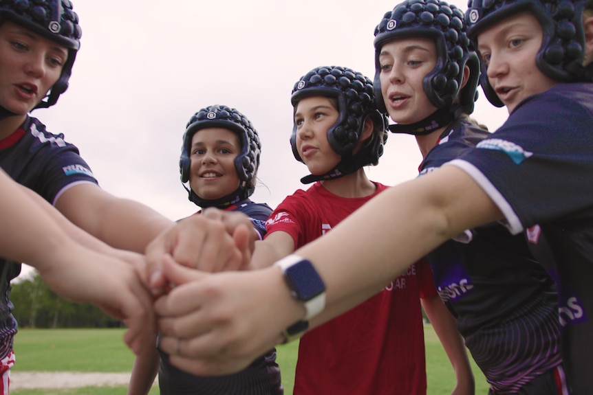 A group of girls wearing black helmets put their hands in.