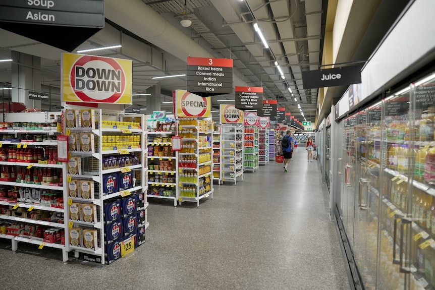 A wide shot of shopping centre aisles in a coles with cold fridges to the right and signs saying Down Down.