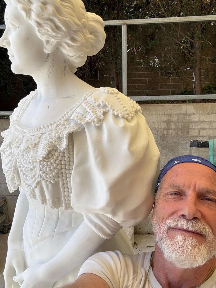 A man poses with a marble sculpture of a woman.