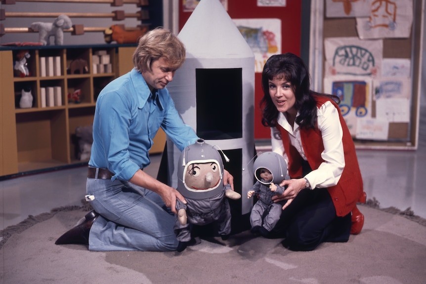 a man and a woman crouch in front of toy rocket ship.