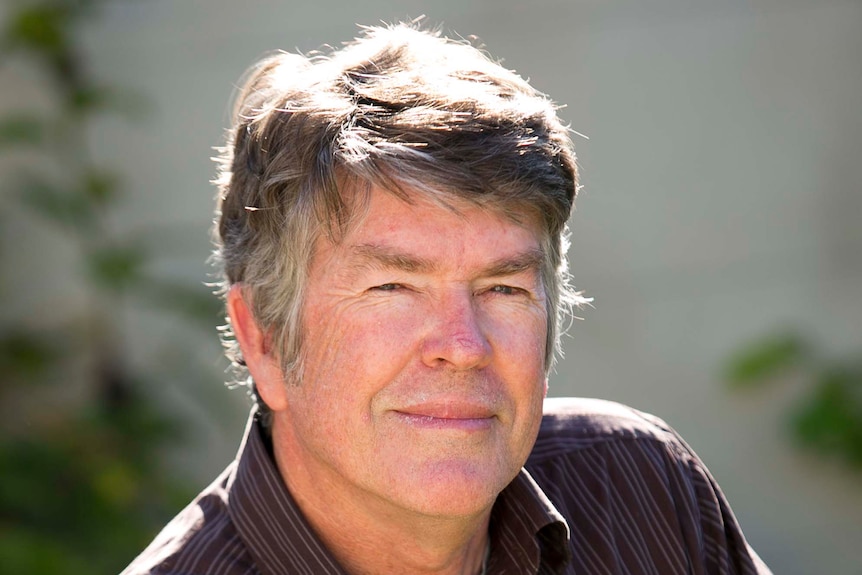 A man wears a dark shirt and smiles.