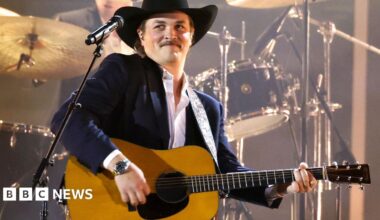 Zach Top pictured wearing a black cowboy hat while holding his Grammy Award trophy