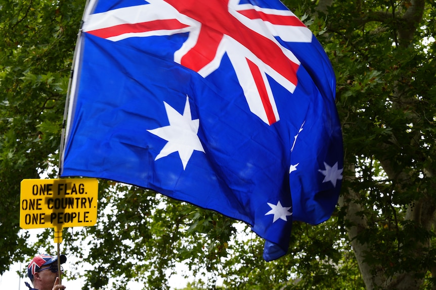 A group of protesters at a park carrying Australian flags and signs.