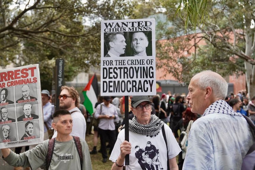 Person in a white t-shirt stands holding a sign