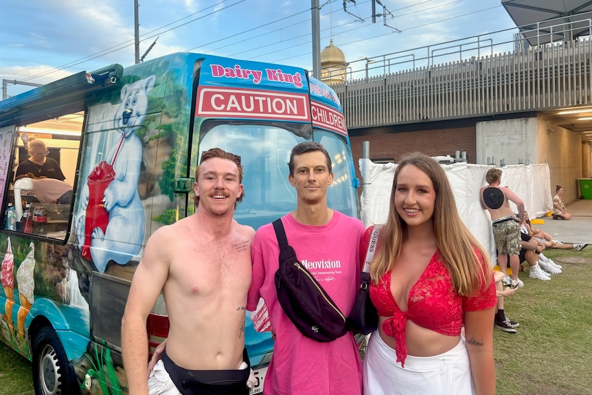 Adam poses for a photo with his arms wrapped around his brother and girlfriend.