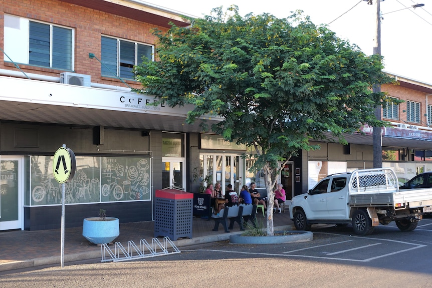 People sitting outside a coffee shop on the bottom floor of a two storey brick building. 