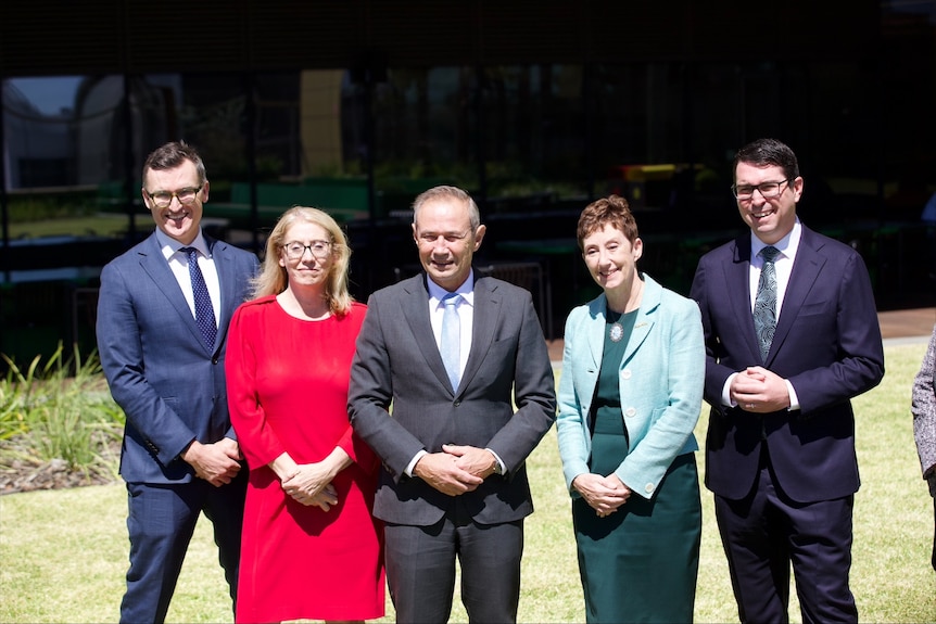 Five people standing side by side for a photo with hands clasped