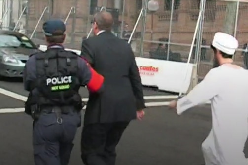 Morrow being led away by police during the APEC stunt, while Licciardello follows behind, dressed as Osama Bin Laden.