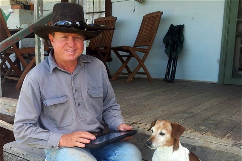 A man wearing a black cowboy style hat sititng next to a small white dog.