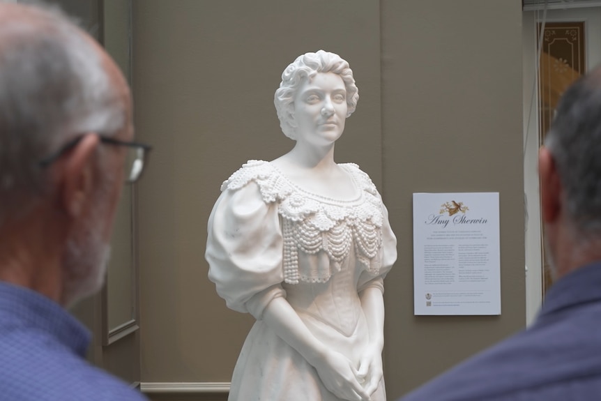 View of two men looking at a marble statue of a woman.