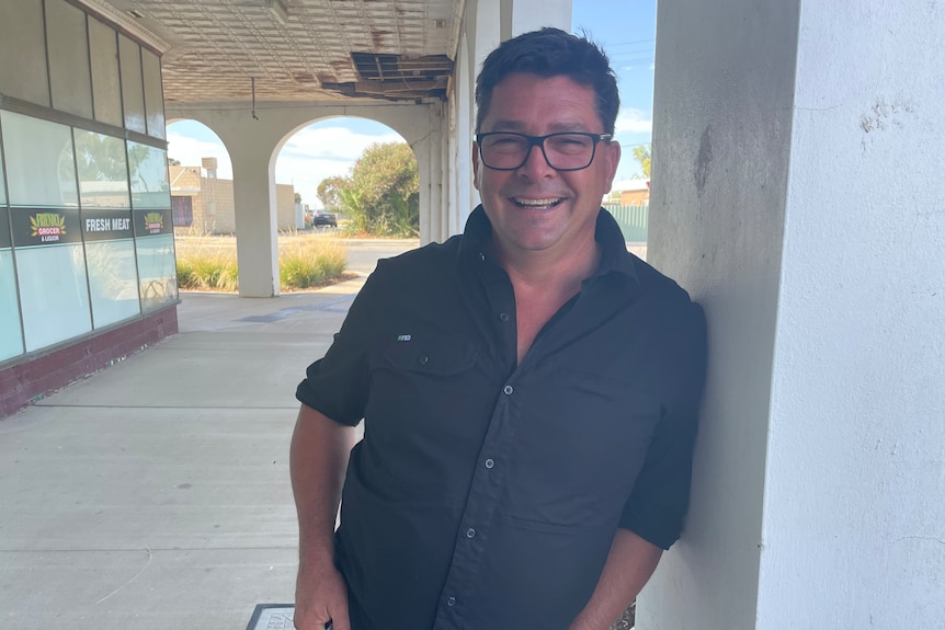 A man with black shirt leaning on a pillar of a white store/facade