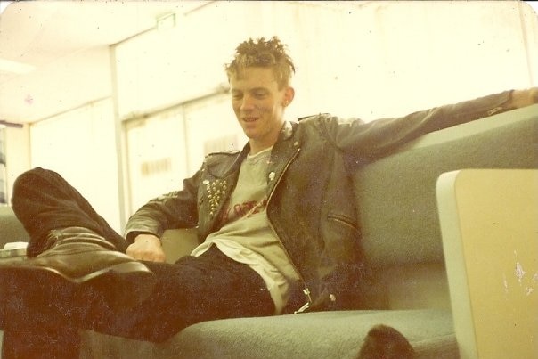 A photo from the 80s of a man sitting on a couch dressed in punk clothing