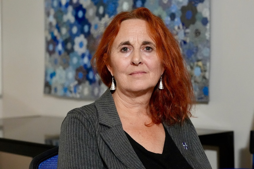 A woman with long red hair in a grey jacket and black top with drop down earrings in an office.