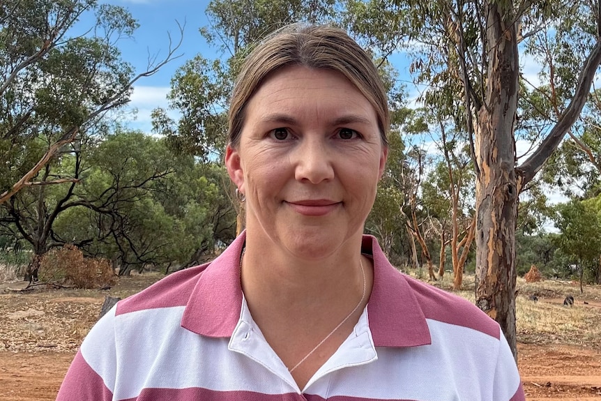 A woman stands in a bush paddock looking at the camera.