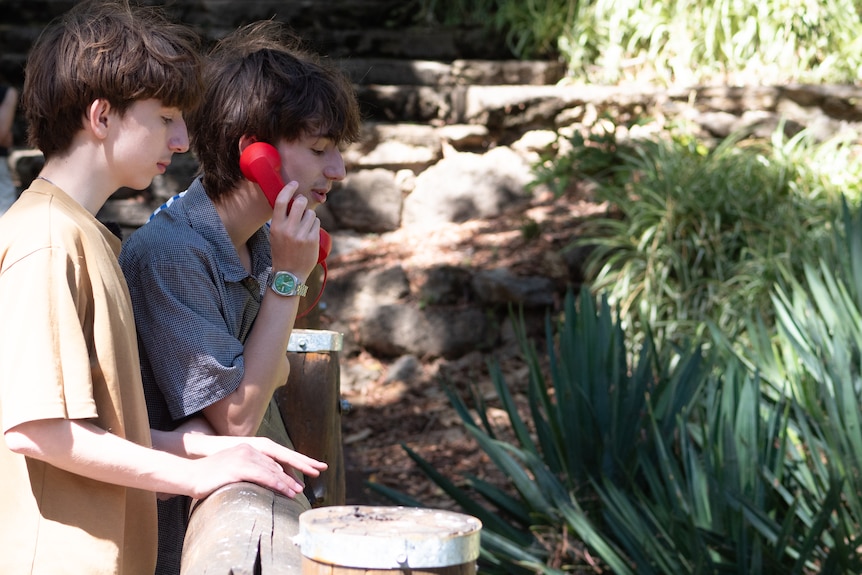 Teen boys stand on a wooden bridge over a pond