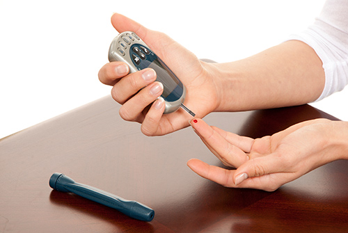 Unseen woman pricking their finger to test their blood sugar level to test for high blood sugar that can be a sign of prediabetes or type 2 diabetes