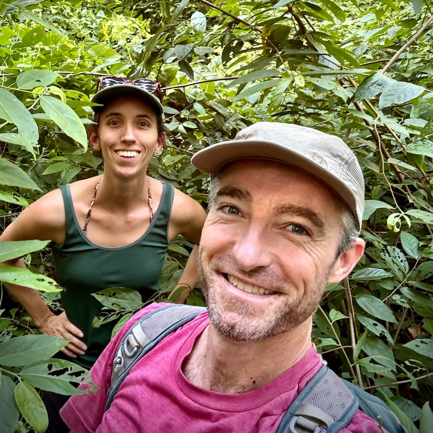 A young couple smile for a selfie amidst thick jungle.