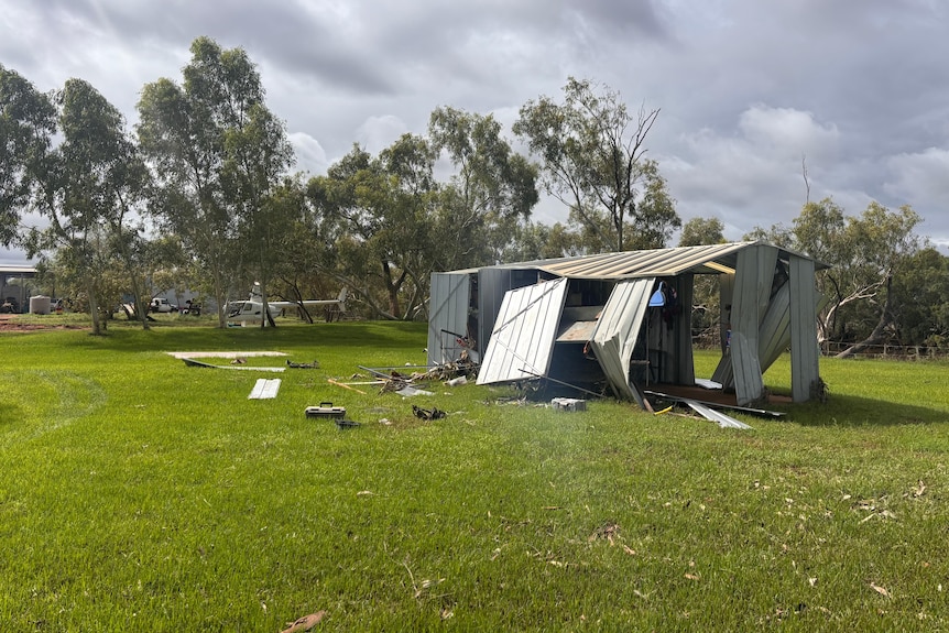 A damaged shed sitting on green grass.