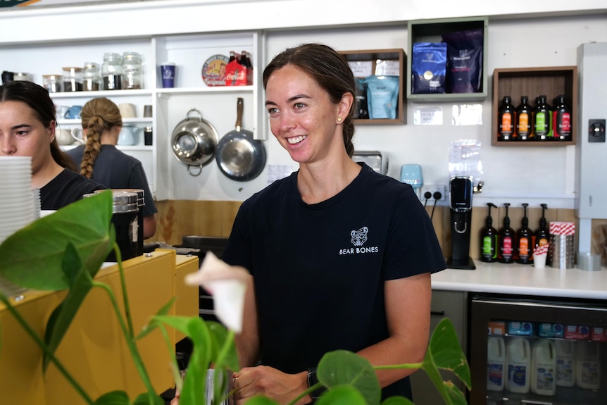 April stands behind the counter at a coffee machine looking out and smiling. 