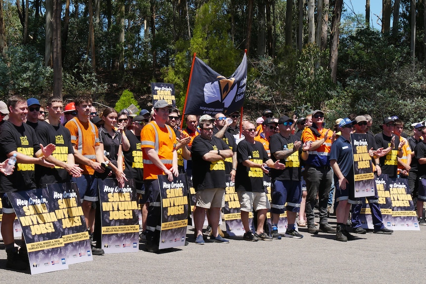 A crowd of men wearing high vis and black shirts holding signs that say 'sav Myuna jobs'