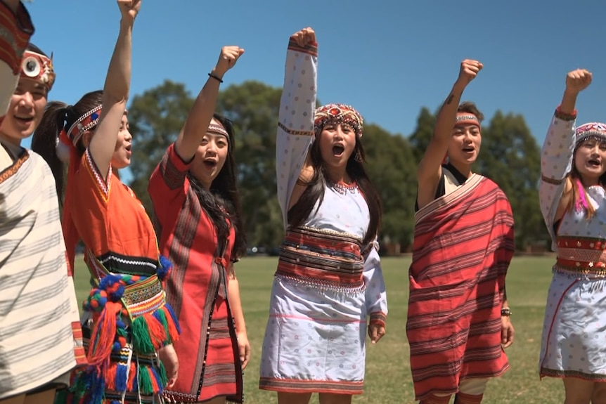 Six Taiwanese-Australians wearing traditional dress have their arms raised in the air, cheering
