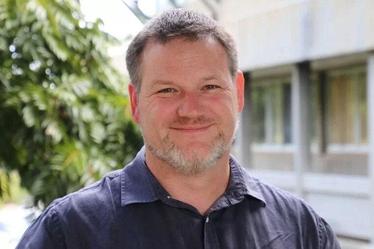 A male university academic stands outside a building.