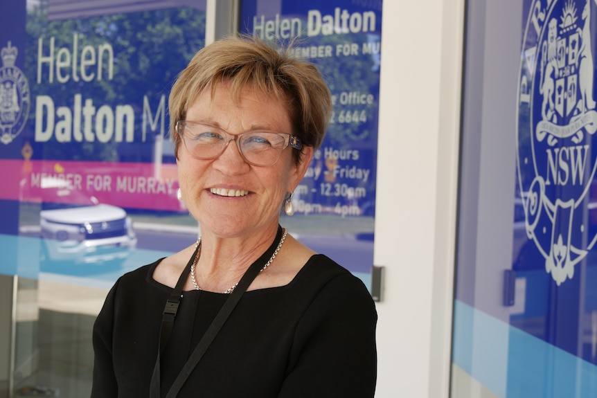A woman in a black dress stands in front of a building smiling