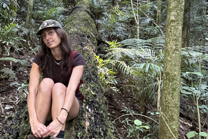A smiling young woman sits on a log in the forest.